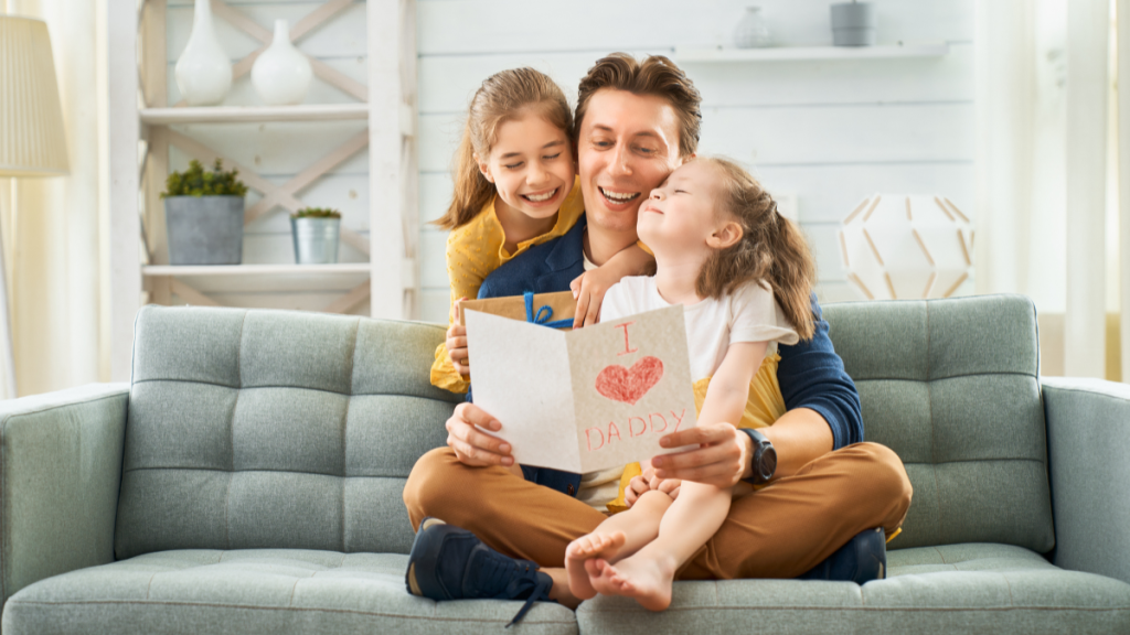 Dad sitting on couch looking at card with daughters.