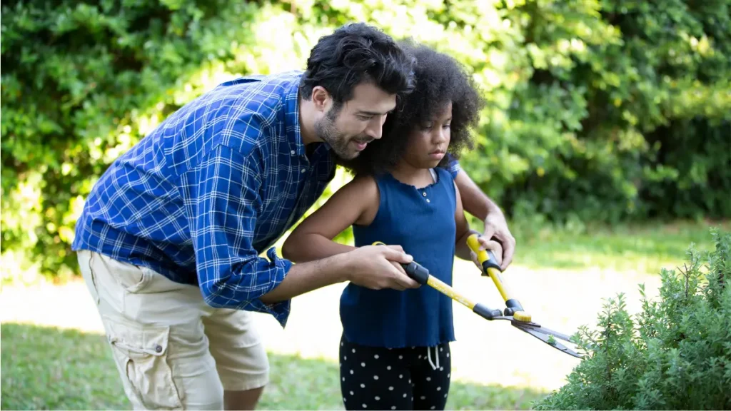 Dad trimming bush with daughter.